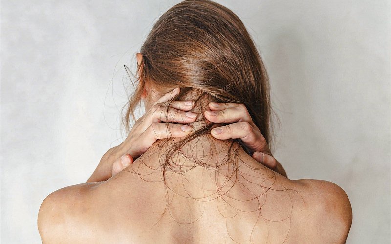 Back view of woman touching her thinning hair.