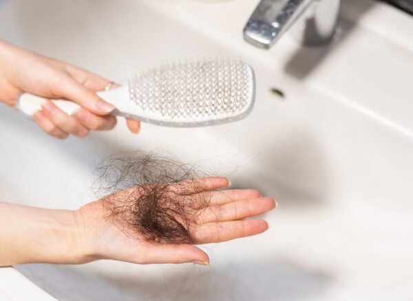 Hand holding fallen hair clump next to hairbrush.