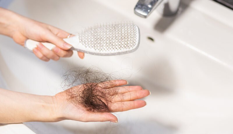 Hand holding fallen hair clump next to hairbrush.