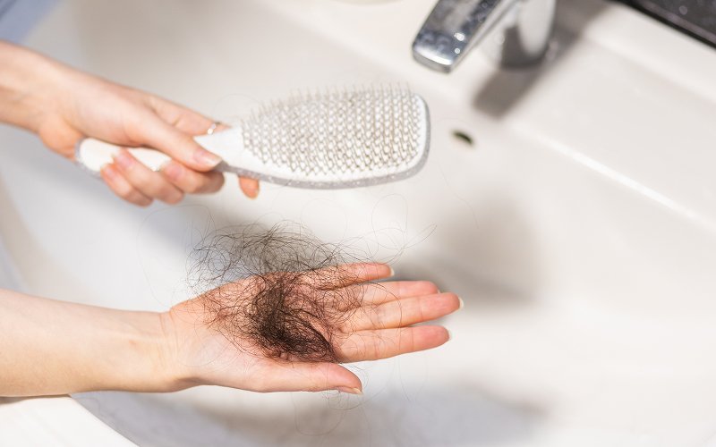 Hand holding fallen hair clump next to hairbrush.