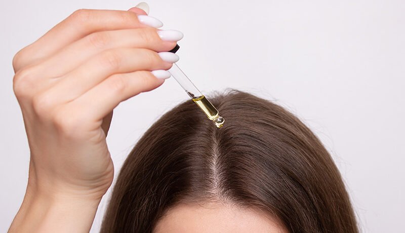 Applying hair growth oil drops directly onto scalp parting.
