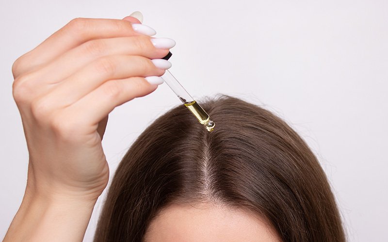 Applying hair growth oil drops directly onto scalp parting.