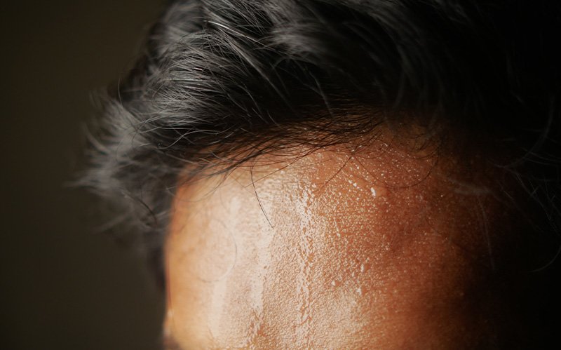 Close-up of forehead and hairline with heavy perspiration drops.