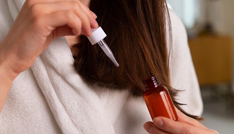 Woman applying oil to hair strands with a dropper.