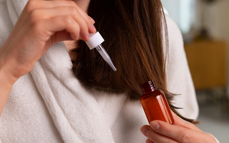 Woman applying oil to hair strands with a dropper.