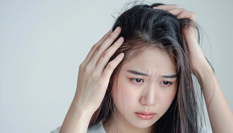 Concerned young woman checking her thinning hair and scalp.