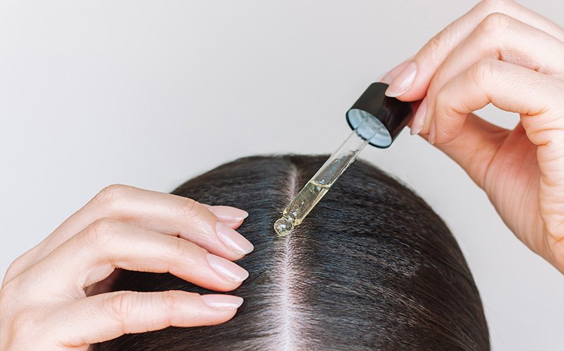 Hand applying nourishing scalp serum directly onto scalp parting.