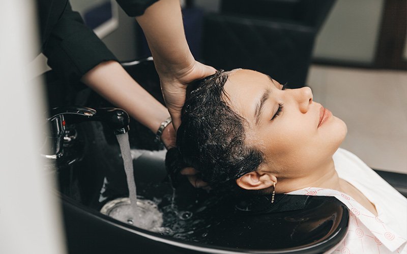Woman enjoying professional scalp treatment wash at hair salon.