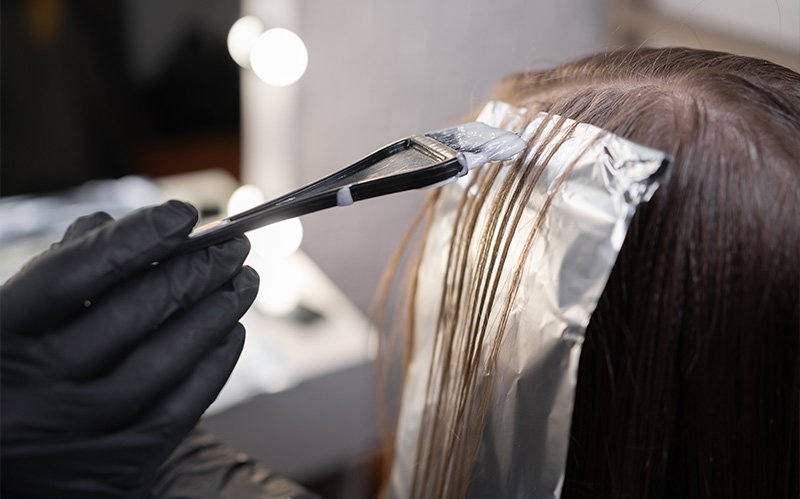 Stylist applying organic hair colour treatment using brush and foil.