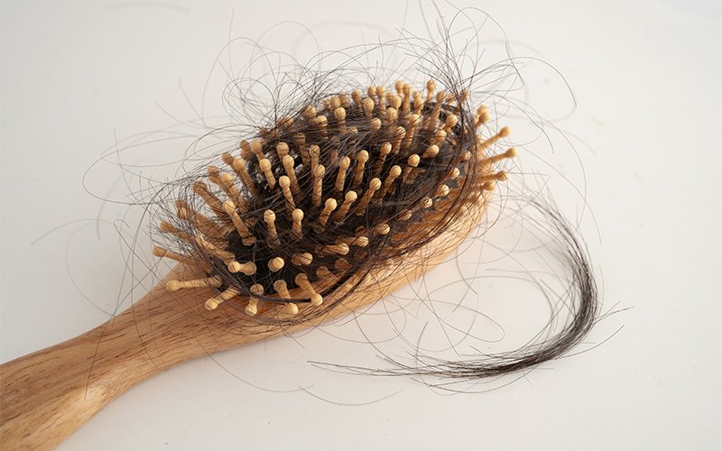 Wooden hairbrush showing signs of excessive daily hair loss.