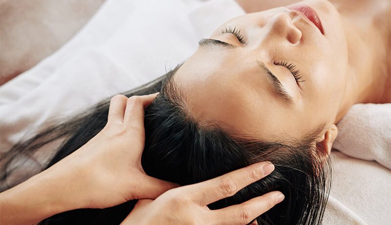 Woman receiving relaxing head massage to improve scalp microcirculation.
