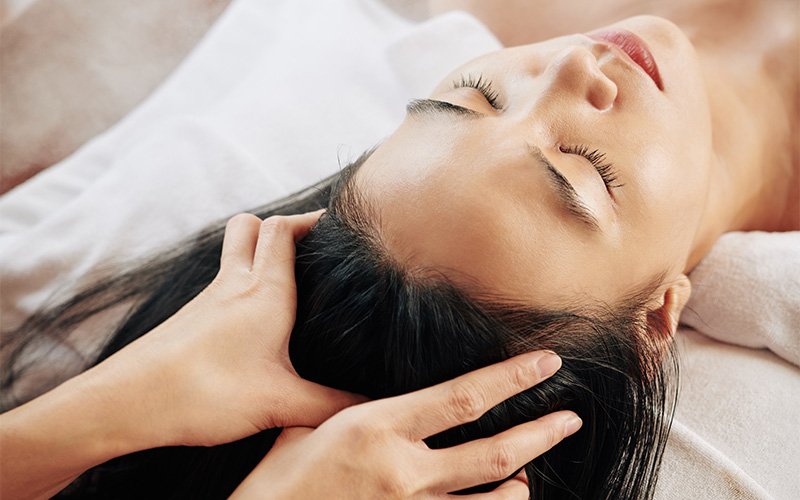Woman receiving relaxing head massage to improve scalp microcirculation.
