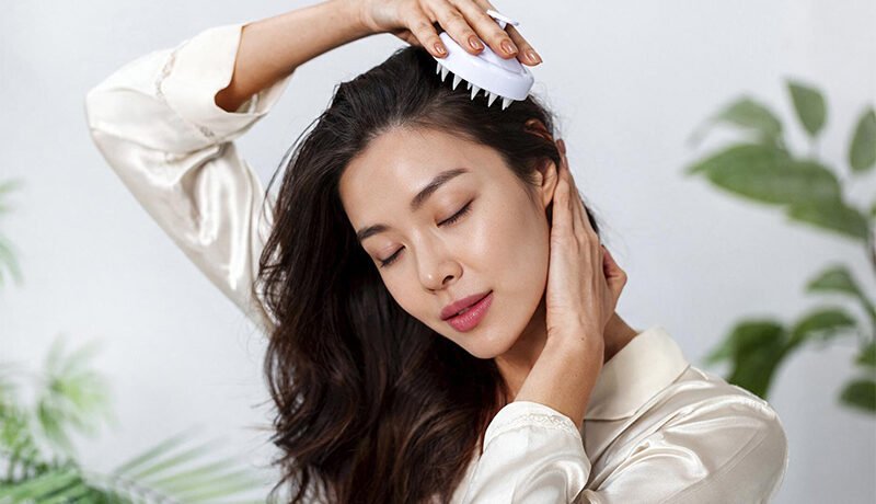 Woman using a scalp massager brush for gentle exfoliation.