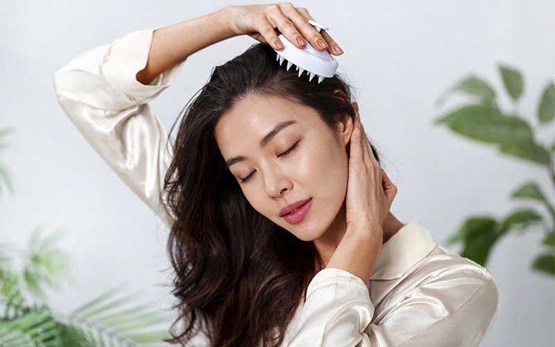 Woman using a scalp massager brush for gentle exfoliation.